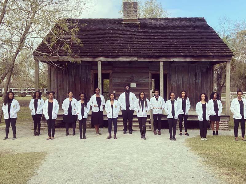 The 15 White Coats stand in front of former plantation slave quarters