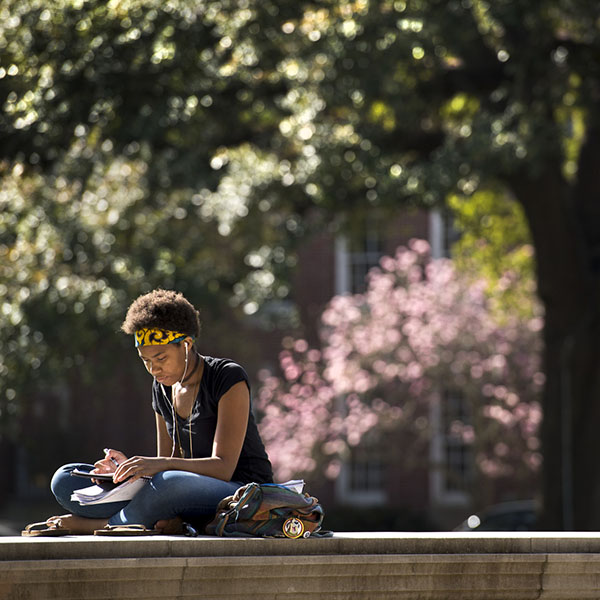 A student sitting outside reading with trees in background