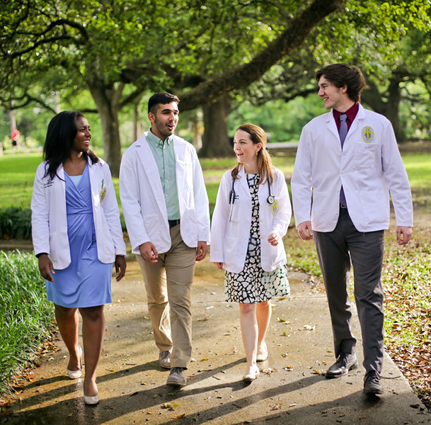 Four students in medical white coats walking together through a park