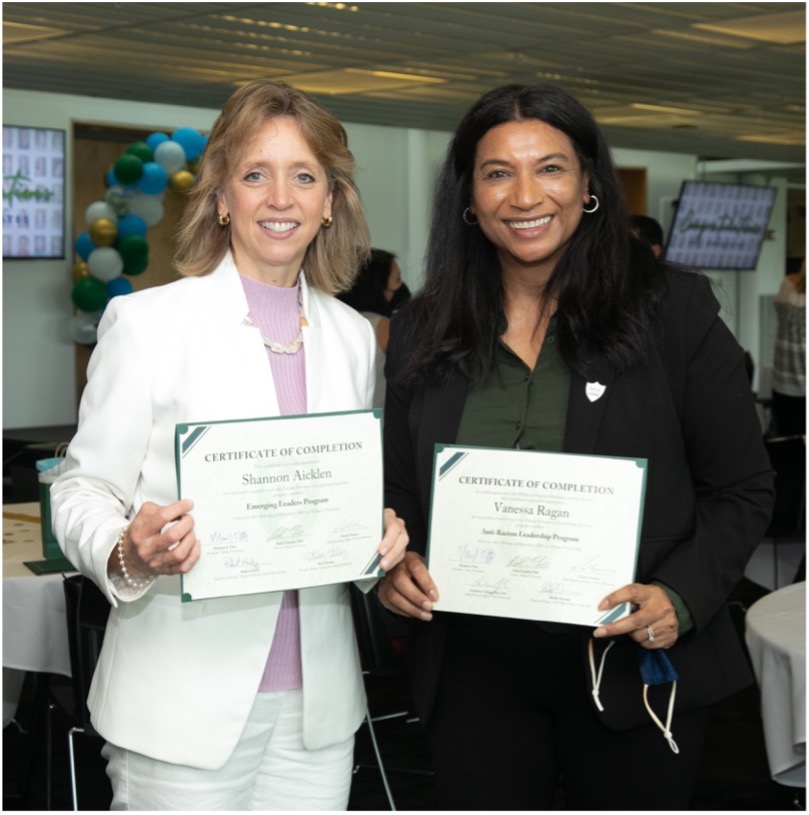 Two staff members hold program certificates