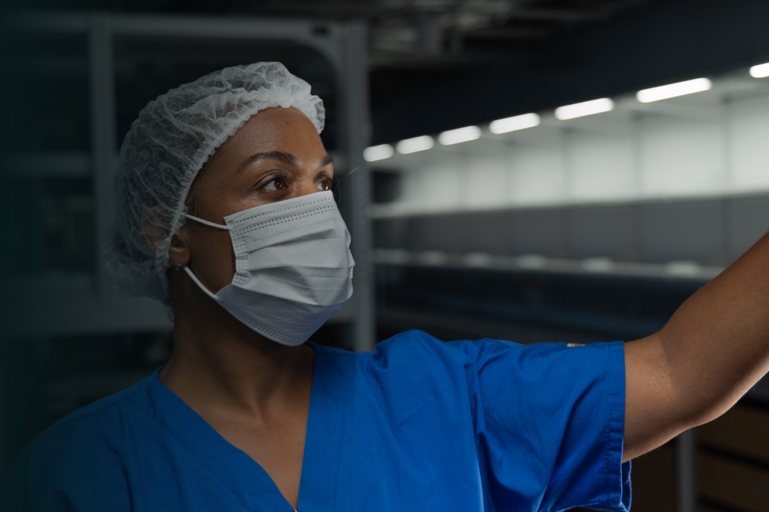 Photograph of a female healthcare worker in a blue scrub and hairnet wearing a white face mask.