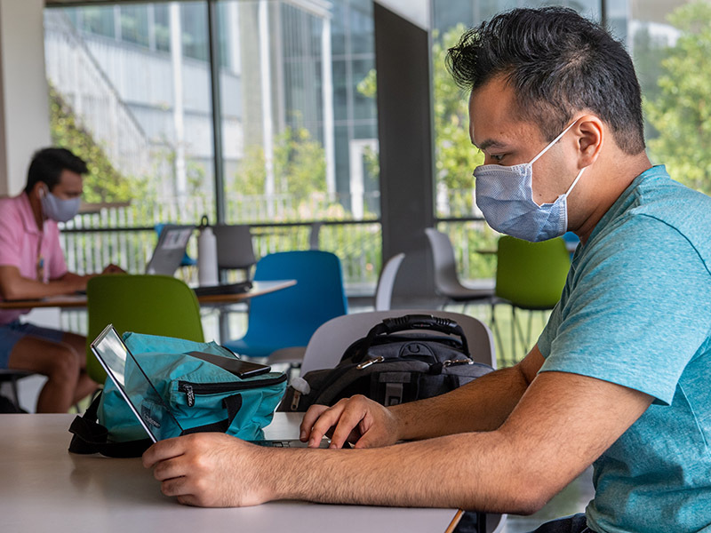 A masked student works from his laptop in the Lavin-Bernick Center