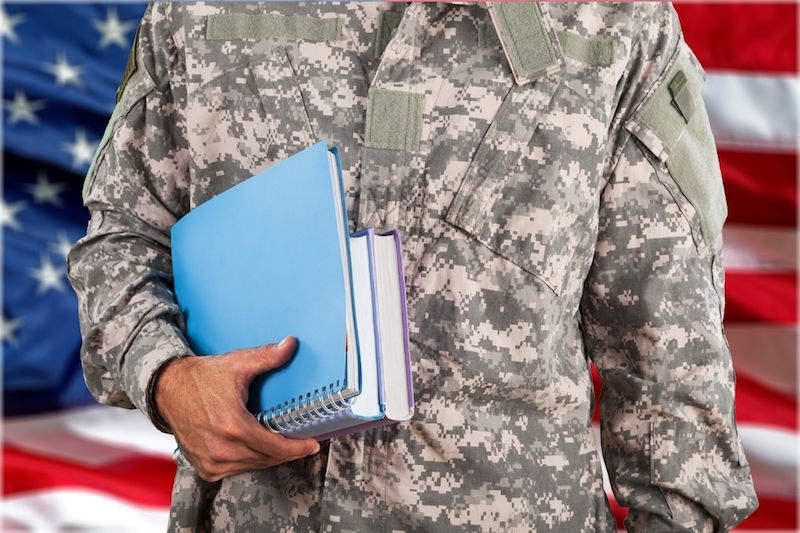 Photo of a serviceman carrying books in front an American flag 