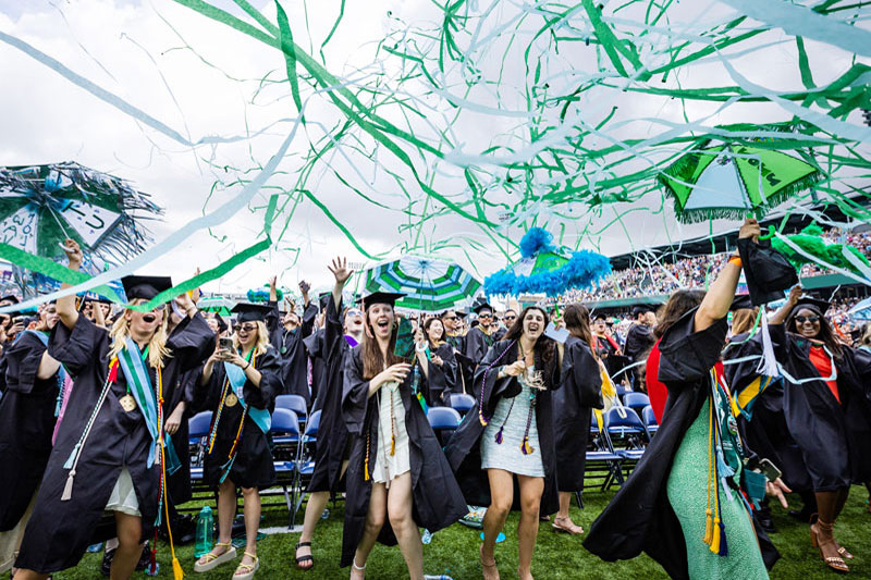 Graduates celebrate with umbrellas and streamers at Yulman Stadium