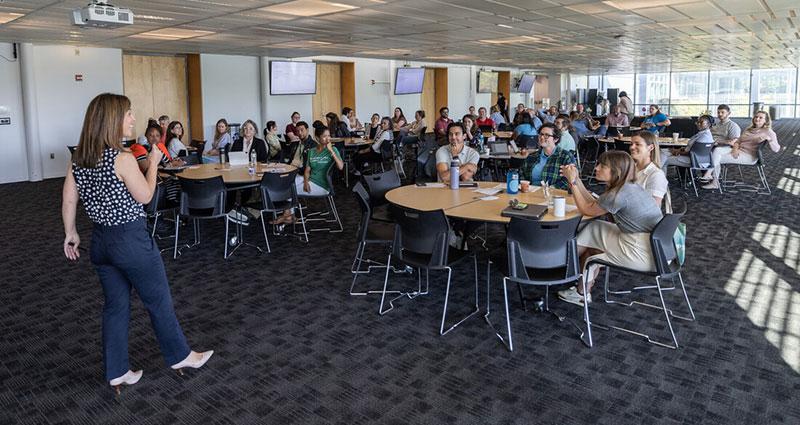 Woman presenting to a room full of Tulane employees seated at round tables.