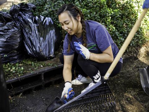 A female student uses a shovel to help clear a rain gutter. 