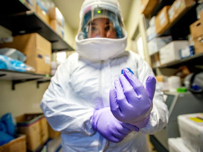 Researcher puts on gloves and safety suit before entering COVID lab