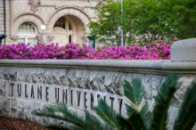 Tulane University stone sign with pink flowers and a campus building.