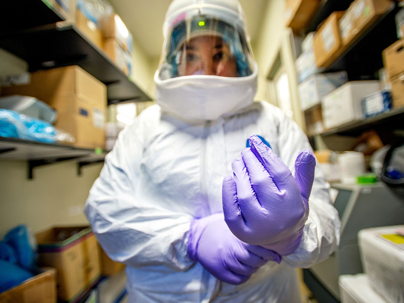 Researcher puts on gloves and safety suit before entering COVID lab